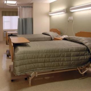 A hospital room with two neatly made beds and medical equipment.