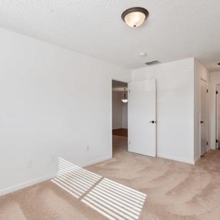 An empty carpeted room with white walls and a ceiling light fixture, featuring an open doorway.