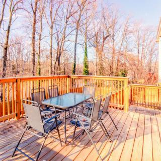 A sunny wooden deck with a glass-top table and chairs, surrounded by trees.