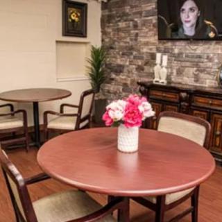 A cozy interior featuring a round wooden table with chairs and a floral centerpiece in a vase, set against a textured brick wall adorned with artwork.