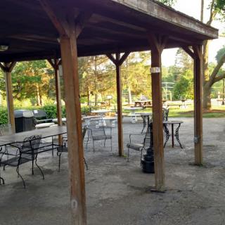 A serene picnic area under a wooden pavilion, surrounded by greenery.