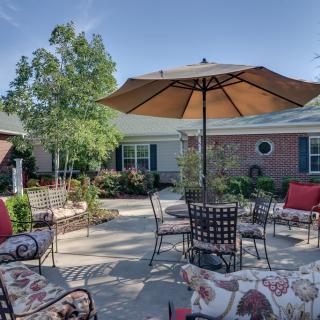 A sunny patio area with outdoor furniture and an umbrella, surrounded by a garden.