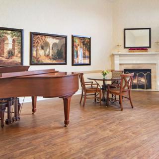 A cozy living room with a grand piano, elegant artwork, and a warm fireplace.