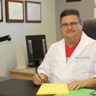 A doctor sitting at a desk in an office, surrounded by papers and certificates on the wall.
