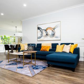 A modern living room featuring a blue sectional sofa with yellow pillows, complemented by abstract wall art and a geometric rug.