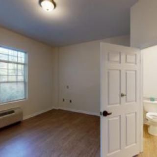 An empty room with wooden flooring and an adjoining bathroom.