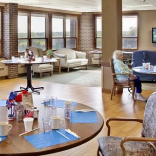 A cozy dining area in a nursing home with tables set for meals and windows providing natural light.