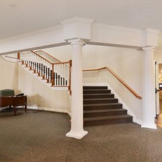 Spacious interior featuring a staircase with elegant columns and carpeted flooring.