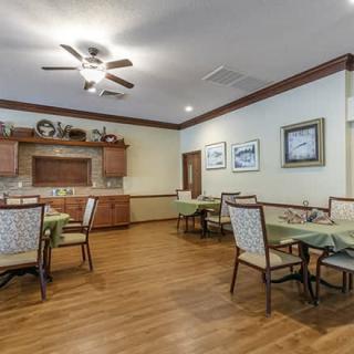 A cozy dining room with neatly arranged tables and chairs, complemented by warm wooden flooring and a ceiling fan.
