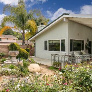 A well-maintained backyard with a patio and lush garden, featuring palm trees and various plants.