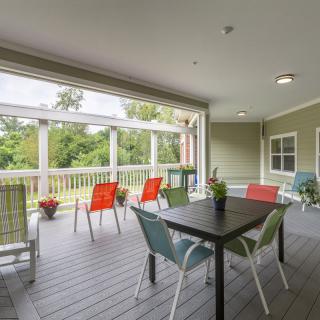 A cozy covered patio with colorful chairs and a table overlooking a lush garden.