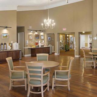 A spacious dining area with round tables and chairs, featuring a chandelier and hardwood flooring.