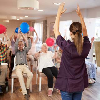A group of seniors participating in a lively exercise session using balloons, led by an instructor.