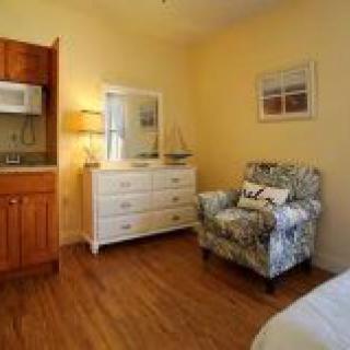 A cozy bedroom with a floral armchair, white dresser, and warm lighting.