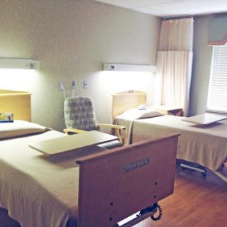 A view of a hospital patient room featuring two beds and a comfortable chair.