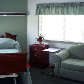 A hospital room with a bed, side table, and sofa near a window.