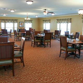 An empty dining room with neatly arranged tables and chairs, carpeted flooring, and overhead lighting.