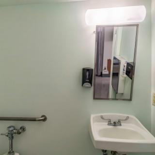 A simple bathroom setup with a sink, mirror, and handrail.