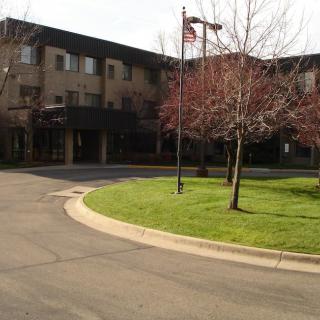 A building with an American flag in front, surrounded by a road and landscaping with trees and grass.