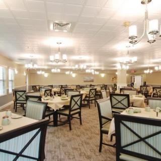 A spacious dining room with neatly arranged tables and chairs, illuminated by elegant lighting.
