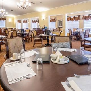 An elegant dining room with neatly set tables and comfortable chairs, featuring chandeliers and a warm ambiance.