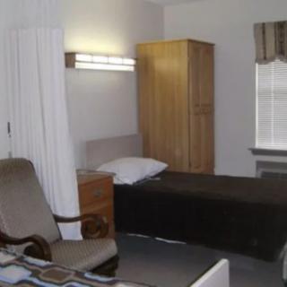 A simple bedroom with a bed, chair, and wardrobe.