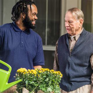 Two individuals engage in a friendly conversation while gardening, surrounded by vibrant flowers.