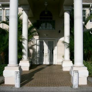 A symmetrical building entrance featuring tall white columns and lush greenery.