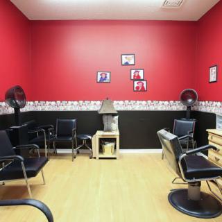 An interior view of a hair salon with red walls and multiple chairs arranged for clients.