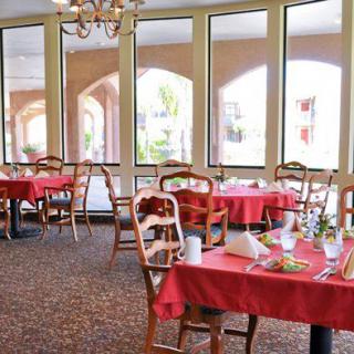 A cozy dining area with tables covered in red tablecloths, set against large windows.