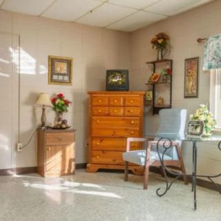 A cozy room featuring a wooden dresser, a blue chair, and various decorative elements including framed pictures and plants.