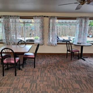 An empty dining area with tables and chairs by large windows adorned with curtains.