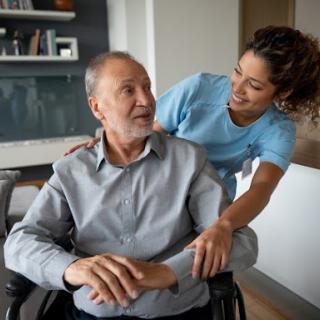 A caregiver interacts warmly with an elderly man in a wheelchair, providing support and companionship.