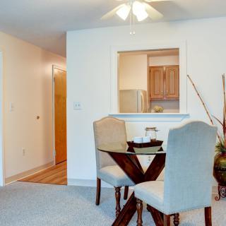 A cozy dining area with a small table and chairs adjacent to an open kitchen in an apartment.