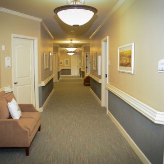 A well-lit hallway with carpeted floor, featuring chairs and artwork on the walls.