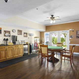A cozy room with a coffee station and a round dining table surrounded by chairs, featuring wood flooring and large windows letting in natural light.