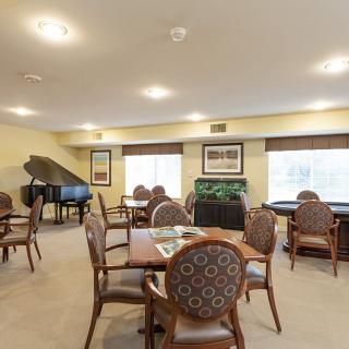 A cozy dining room with tables, chairs, and a grand piano.