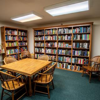 A cozy library reading room with wooden bookshelves filled with books and a table surrounded by chairs.