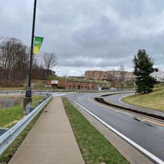A winding road with a sidewalk and greenery under a cloudy sky.