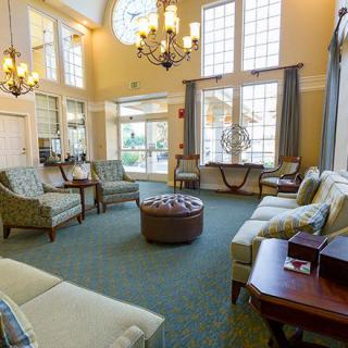 A spacious living room with elegant chandeliers and ample seating, illuminated by natural light through large windows.