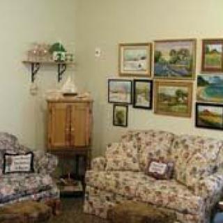A cozy living room with floral-patterned furniture and a collection of paintings on the wall.