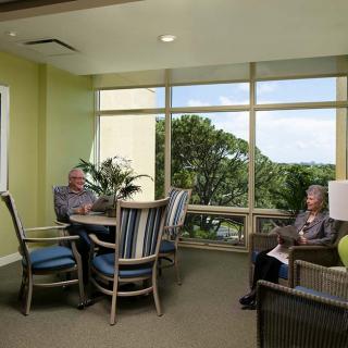 Elderly individuals relaxing in a comfortable seating area with a scenic window view.