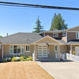 A suburban house with a driveway and garage, surrounded by trees on a sunny day.