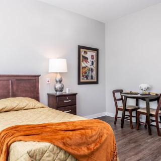 A cozy bedroom with a wooden bed, nightstand, and dining table set in a bright space.