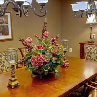 A dining room with a wooden table adorned with a floral centerpiece and elegant chandeliers overhead.