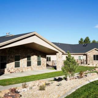 A modern residential house with a stone exterior, set against a clear blue sky and landscaped yard.