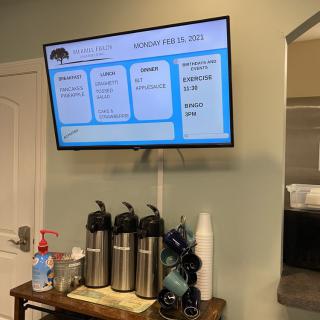 An indoor coffee station setup with a television displaying a schedule above it.