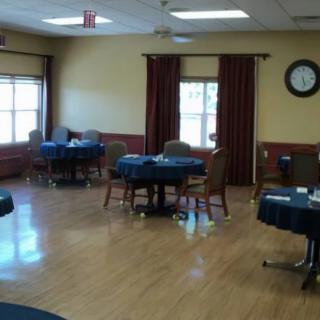 An empty dining room with tables and chairs, featuring windows with curtains and a clock on the wall.
