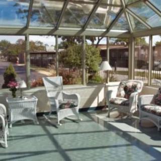 A bright sunroom with wicker furniture and a glass roof, offering a view of the garden outside.