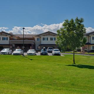 A building with a parking lot in front, surrounded by a grassy area and trees under a clear blue sky.